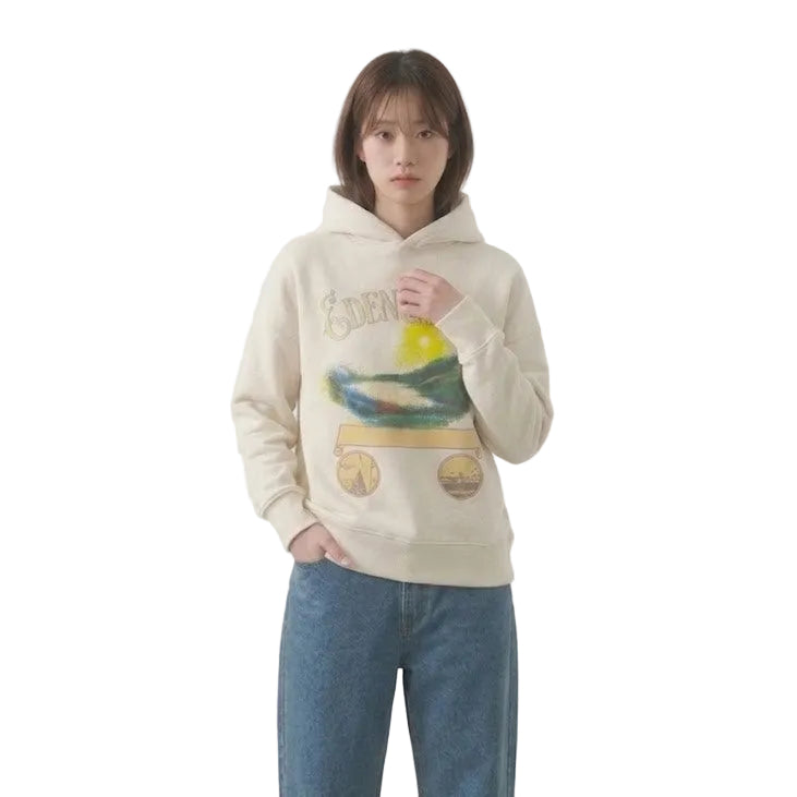 Person wearing a beige hoodie with a colorful design and blue jeans on a plain background