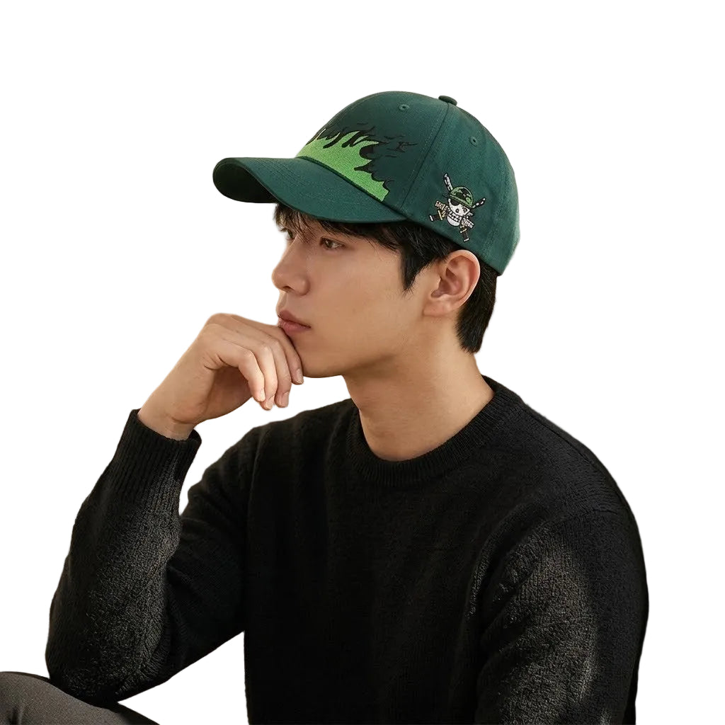 Person wearing a green cap with a design, sitting against a light-colored wall.