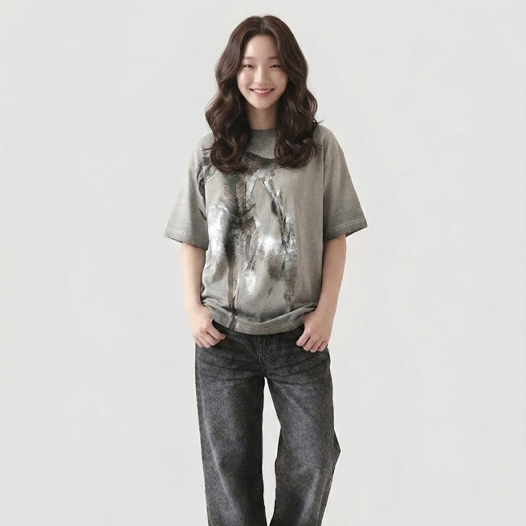 Person wearing a gray t-shirt with a graphic design and dark jeans on a white background