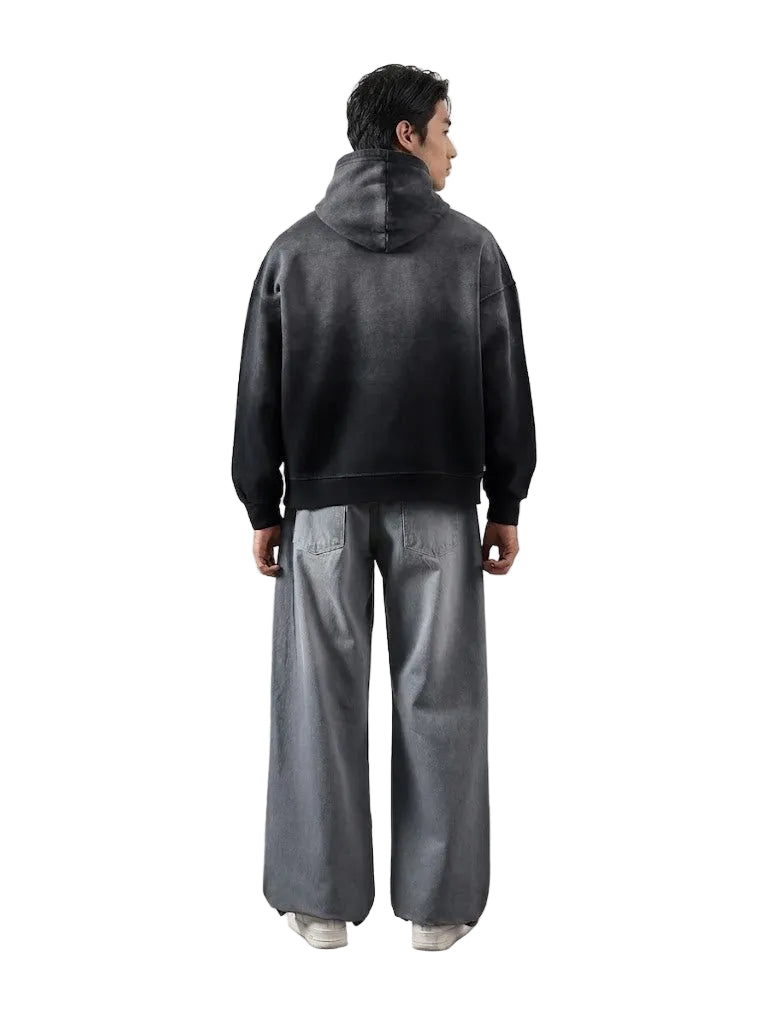Person wearing a black jacket and gray pants standing against a white wall.