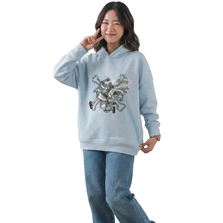 Person wearing a light blue hoodie with a graphic design and blue jeans, standing against a white background.